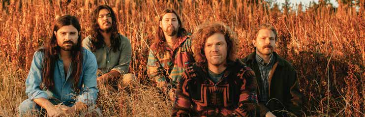 The five members of The Whags seated among tall, dry grasses.
